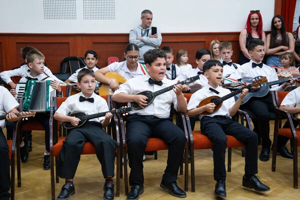Középen ülő fiú énekelve tamburázik, társai, egyik harmonikás, játszanak a Csokonai Rendezvényházban.