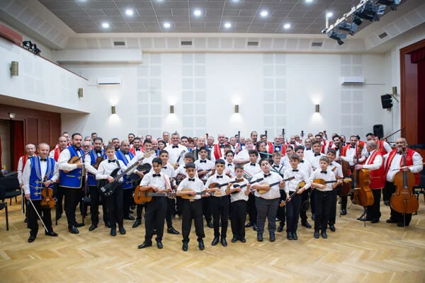 A két zenekar tagjai közös csoportképen állnak hangszereikkel, elöl a gyermek tamburások sorakoznak.