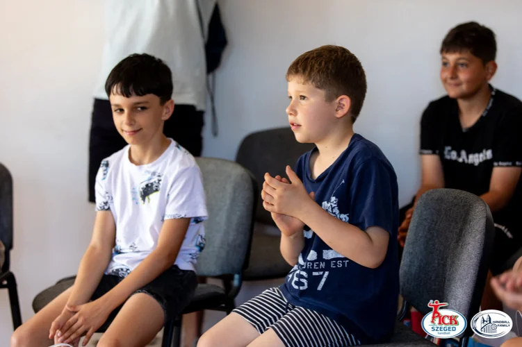 Két fiú ül egymás melletti székeken, egyikük tapsolva figyel a sükösdi teremben