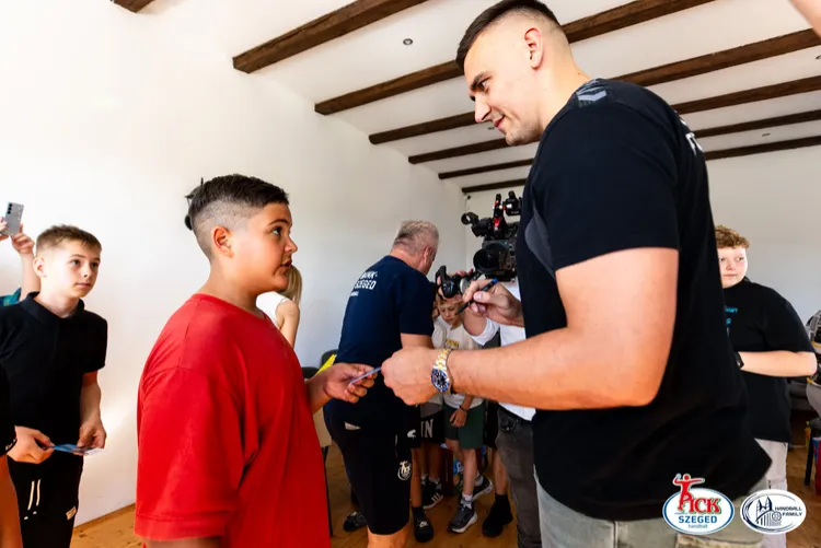 PICK Szeged játékos autogramkártyát ad át egy piros pólós fiúnak a teremben