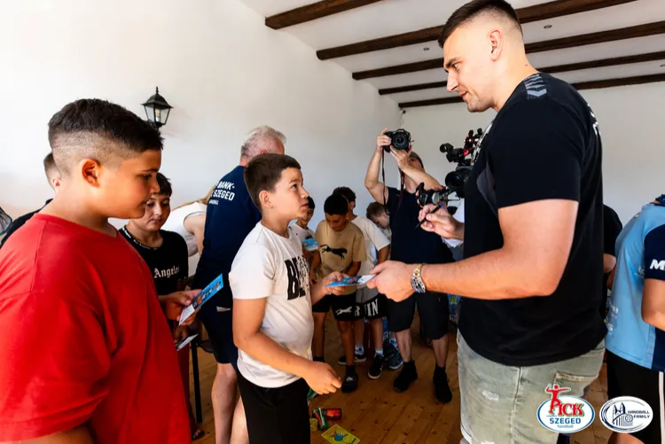 PICK Szeged játékos autogramkártyát ad át egy fehér pólós fiúnak, mögötte várakozó gyerekekkel