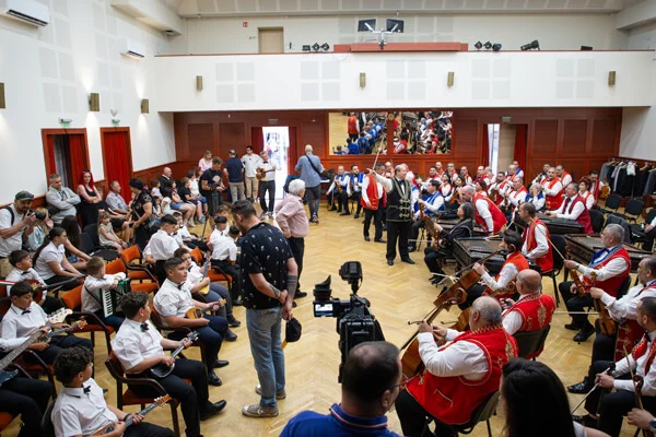 A két zenekar egymással szemben ül, közöttük fotósok és kamerák rögzítik a közös próbát felülnézetből.