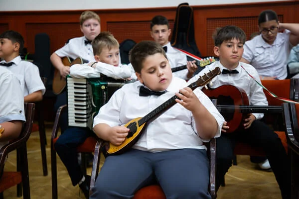 Elöl egy fiú sárga tamburán játszik, mögötte harmonikás, gitáros és nagyméretű tamburás társai ülnek.
