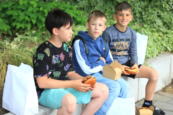 Három fiú ül a Szent István parkban, ketten hamburgert tartanak az országgyűlési fellépés előtt.