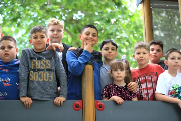 A zenekar fiútagjai közelebbi csoportképen sorakoznak a játszótéren, egyikük játékosan pózol.