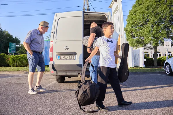 Fehér inges tamburás fiú hangszertokokkal érkezik a furgon mellé a révfülöpi szereplés reggelén.