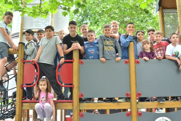 A zenekar gyerektagjai csoportképen sorakoznak a játszótéren, egy kislány az alsó részen ül.