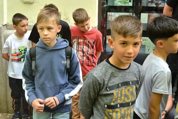 Két fiú áll az előtérben, mögöttük a zenekar további gyerektagjai várakoznak az épületnél.